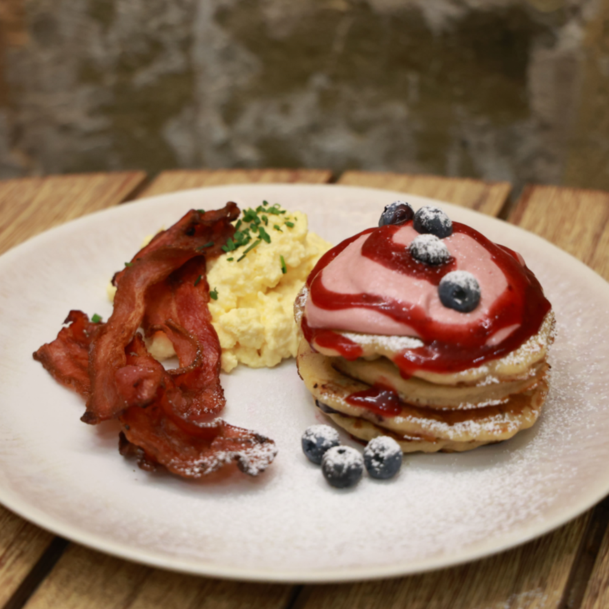 Desayuno americano con bacon, huevos revueltos y pancakes con arandanos